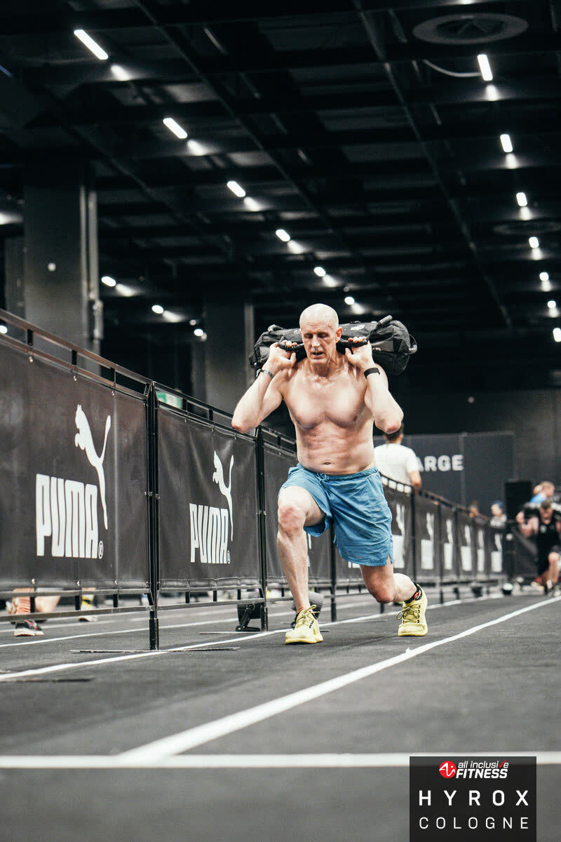 Age-group HYROX athlete carrying a sandbag during lunges